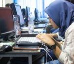 A young woman in hijab using a laptop in a computer classroom setting.