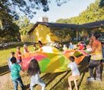 Group of children playing with a colorful parachute outside during a sunny day party.