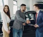 Buyers and sales representative shake hands at a car dealership for a successful car purchase.