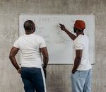 Two adult men planning their gym exercises on a whiteboard in a modern setting, emphasizing fitness and health.